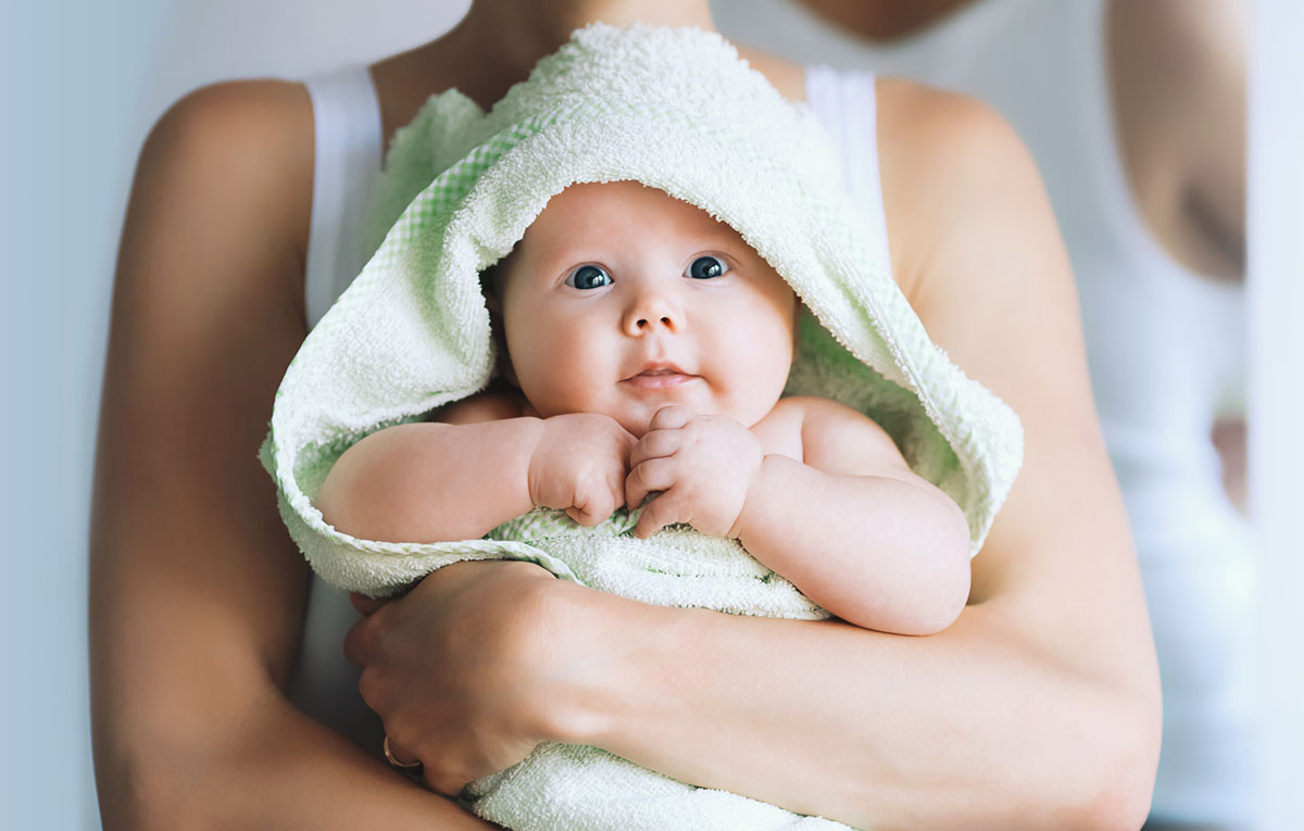 Mother holding her freshly bathed baby in her arms, wrapped in a bright green baby towel as a symbol of the instructions for bathing the baby