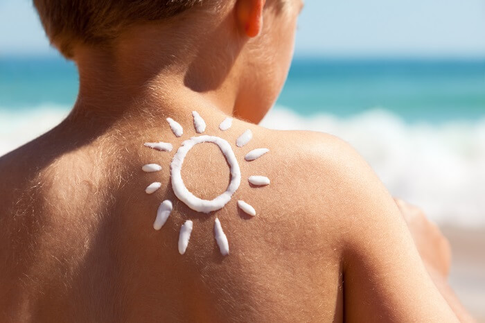 Child sitting on the beach with a sun drawn on their back with sunscreen as a symbol of sun protection for babies and children