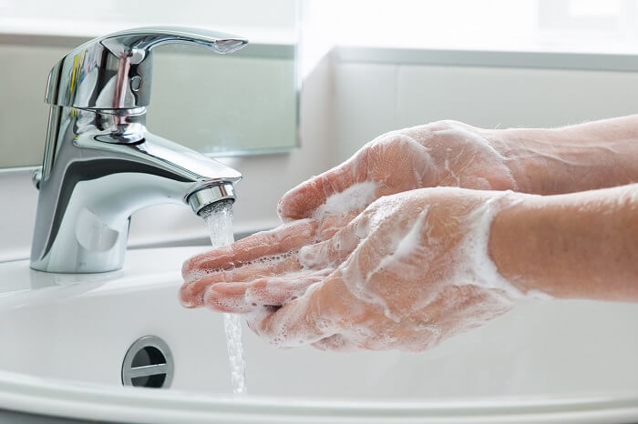 Ein Paar eingeseifte Hände spülen sich den Schaum unter dem Wasserhahn herunter.