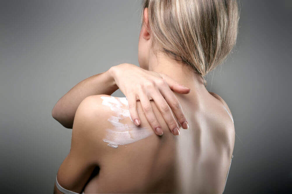 Zu sehen ist der Rücken einer Frau. Sie cremt ihn sich mit der Linola Hautmilch ein.